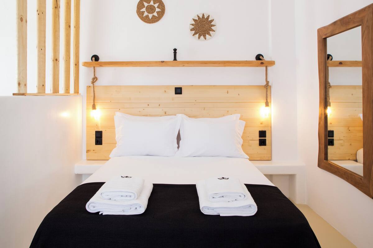 Ein ordentlich bezogenes Bett mit weißen Leinentüchern und zwei gefalteten Handtüchern, ein hölzernes Kopfteil und ein Nachttischregal mit einer kleinen Lampe.