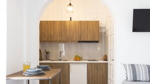 A modern kitchen with wooden cabinets, a white countertop, and a dining area with a table and chairs. - Paros King Luxury Apartments (Paros)