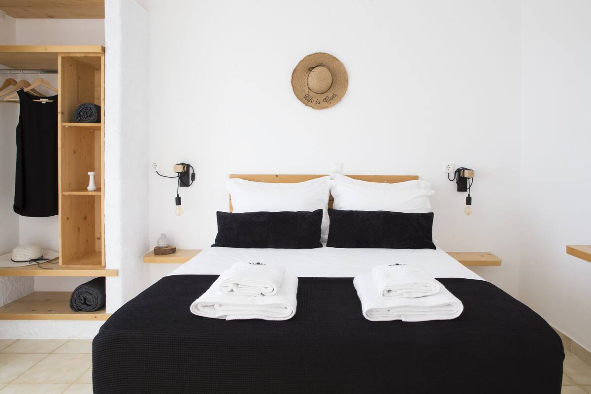 Ein ordentlich bezogenes Bett mit schwarz-weiß gestreifter Bettwäsche, einem Holzkopfschild und zwei weißen, gefalteten Handtüchern.