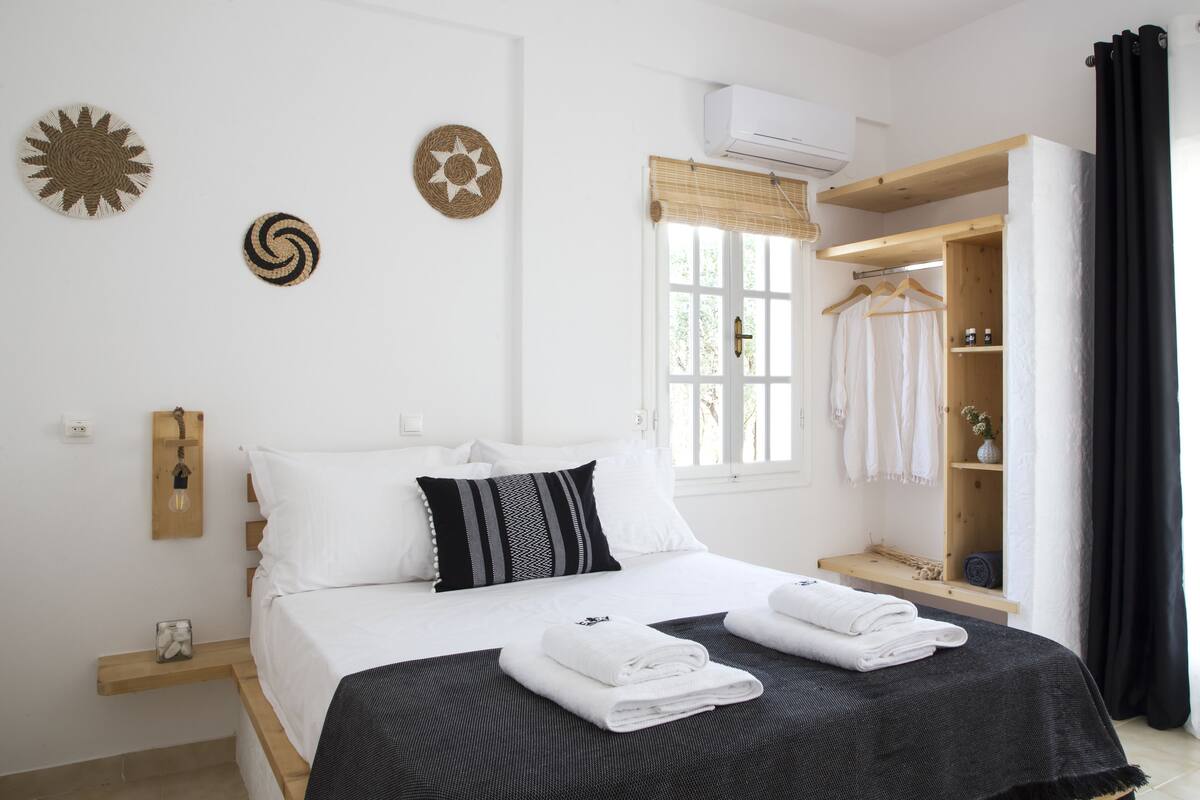 Ein ordentlich eingerichtetes Schlafzimmer mit Bett, Nachttischen, einem Kleiderschrank und einem Fenster mit Vorhängen.