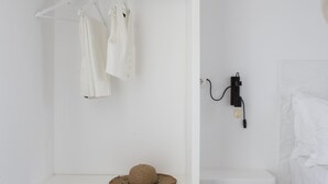 A white wardrobe with a hanging rod, a shelf with a hat, and a wall-mounted light fixture. - Paros King Luxury Apartments (Paros)