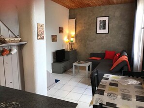 Un salon confortable avec un canapé, une table basse, un téléviseur et une étagère murale où sont posées des tasses.