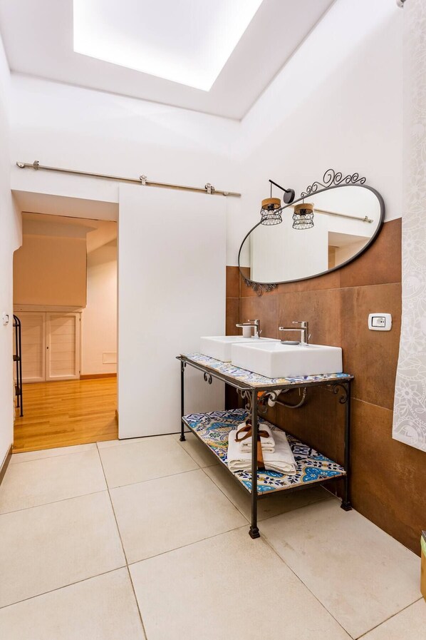 A modern bathroom with a skylight, a white sink, a mirror, and a patterned shelf. - Apartment in the heart of the Ballarò market (Palermo)