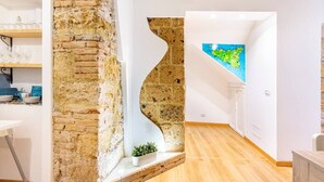 A modern kitchen with a stone accent wall, wooden flooring, and a view of a colorful map on the wall. - Apartment in the heart of the Ballarò market (Palermo)