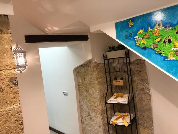A bathroom with a stone wall, a shelf with towels, a map, and a lantern. - Apartment in the heart of the Ballarò market (Palermo)