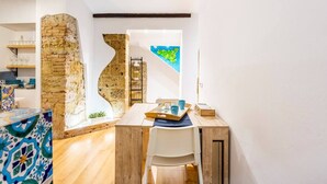 A dining area with a wooden table, a white chair, and a tray with cups and a small plant. There is a stone wall and a map on the wall. - Apartment in the heart of the Ballarò market (Palermo)