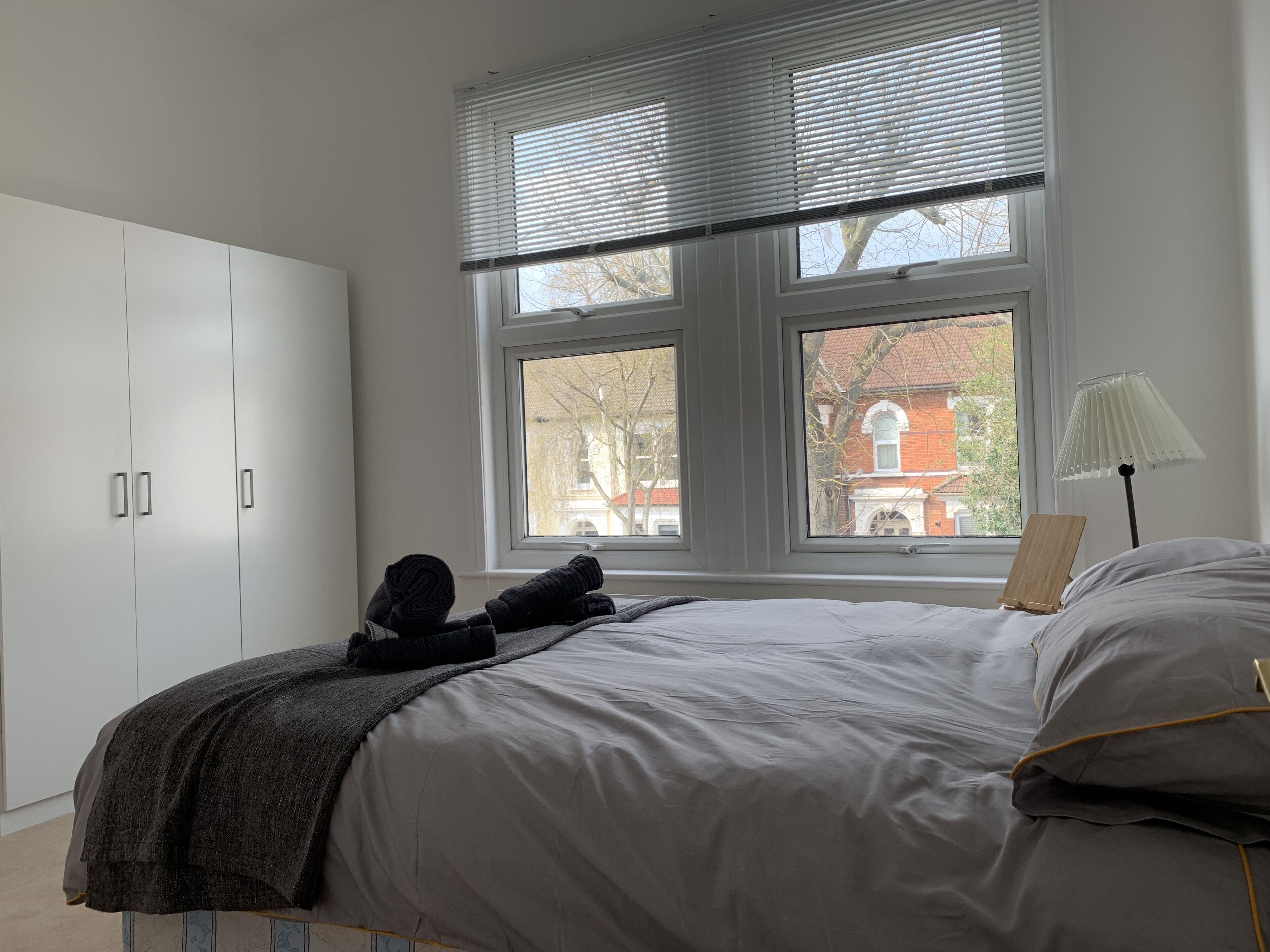 A bedroom with a bed, a wardrobe, and a window with blinds.