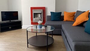 Un salon moderne avec un canapé gris, une table basse en verre, un téléviseur à écran plat posé sur un meuble noir et une cheminée encadrée de rouge.