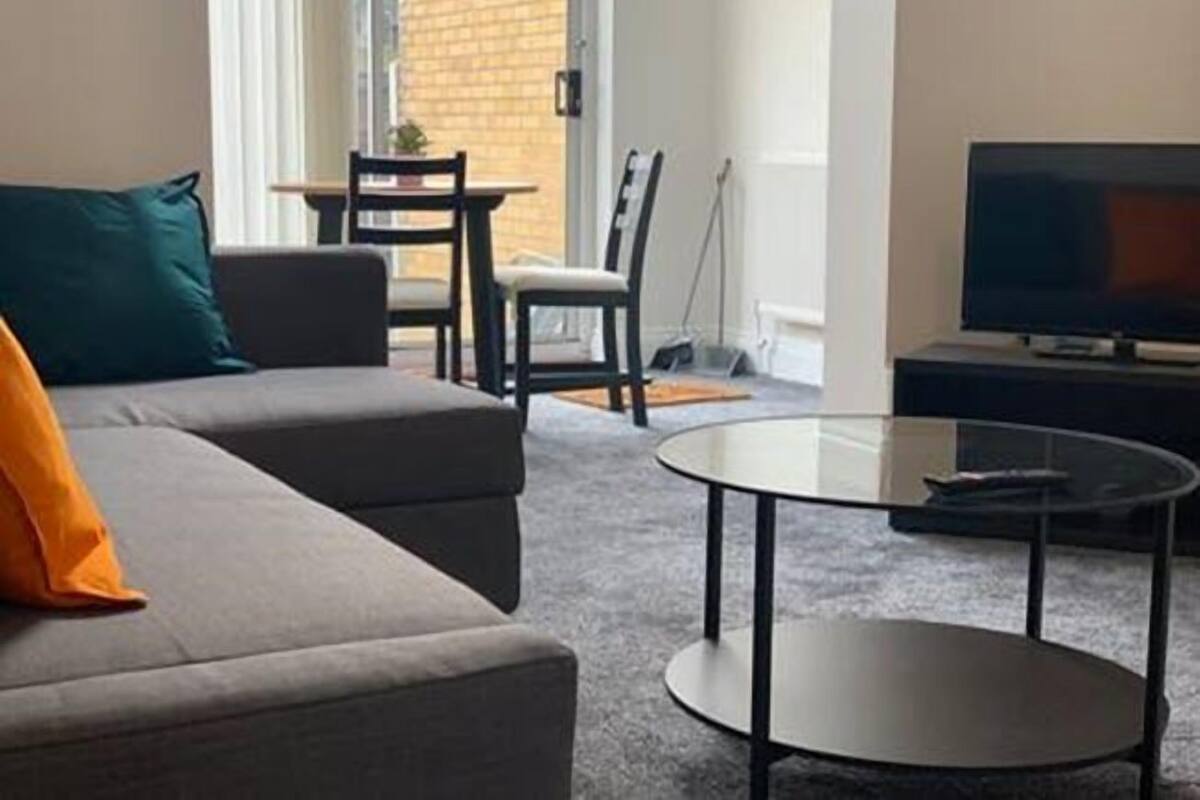 A modern living room with a grey sofa, a glass coffee table, and a television on a stand.