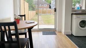 Une cuisine équipée d’un lave-linge, une table à manger avec des chaises et une porte-fenêtre coulissante donnant sur un jardin.