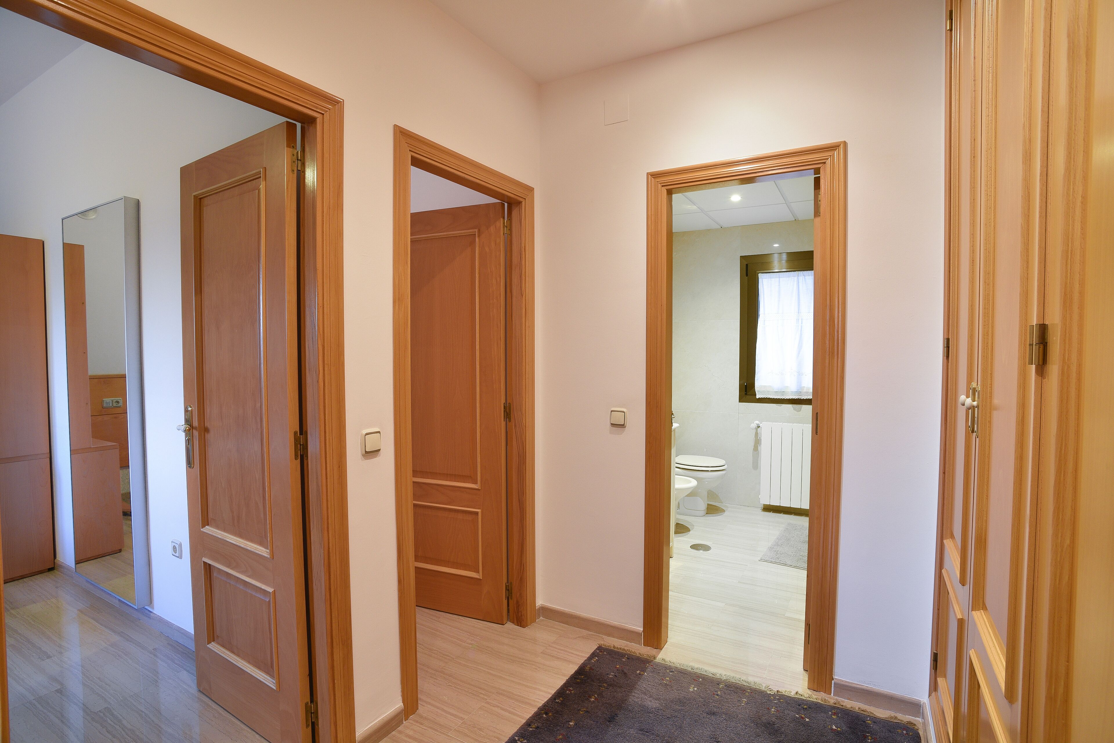 A hallway with wooden doors leading to a bathroom and a bedroom.