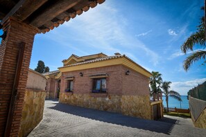 Un edificio tradicional con techo de tejas y paredes de ladrillo, un camino empedrado y vista al mar.