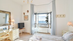 Un dormitorio con cama, escritorio, silla, televisor y vista al mar.