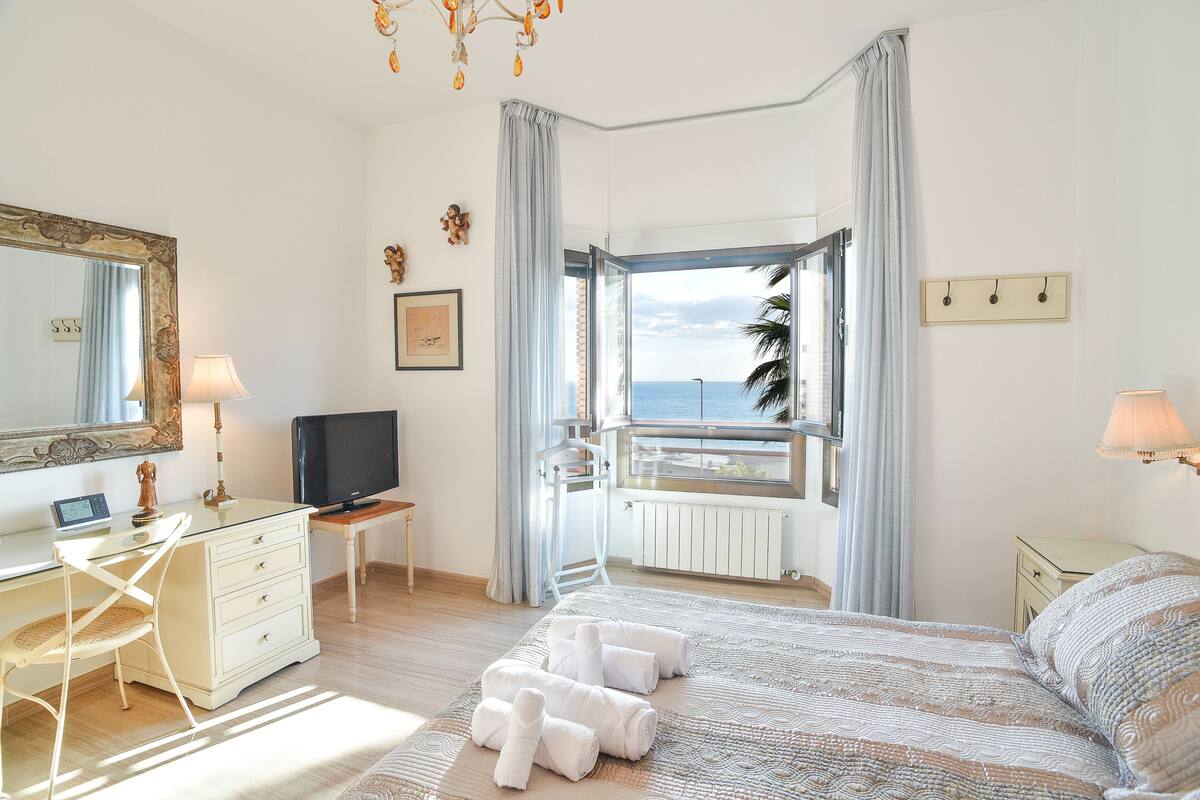 Une chambre à coucher avec un lit, un bureau, une chaise, une télévision et une vue sur la mer.