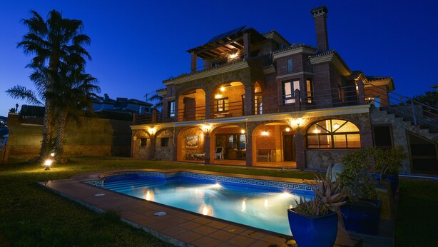 Una casa grande de dos pisos con piscina, ventanas arqueadas y un balcón.