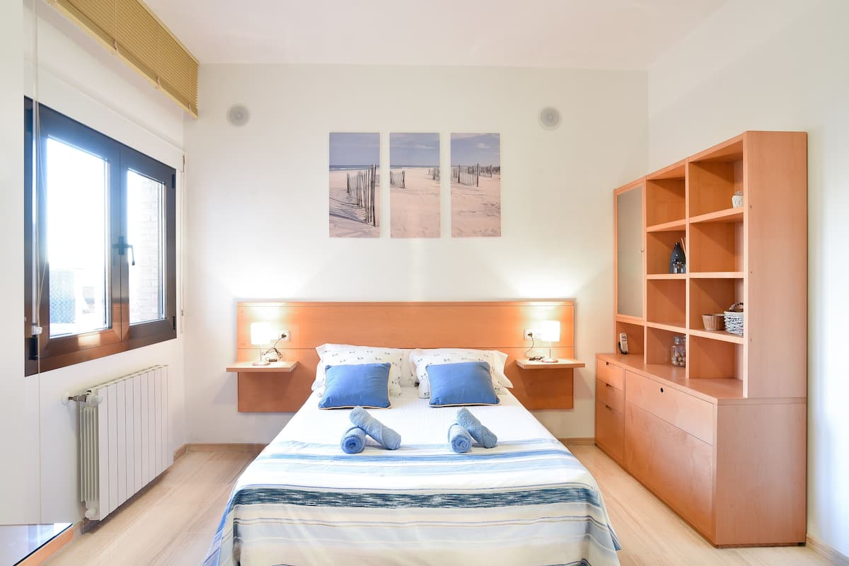 Une chambre d’hôtel comprenant un lit, deux tables de chevet, une armoire en bois et une fenêtre avec des stores.