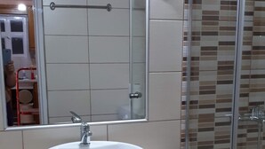 A bathroom with a round white sink, a mirror above it, and a shower area with a glass door. - A nice apartment in corfu town (Corfu)
