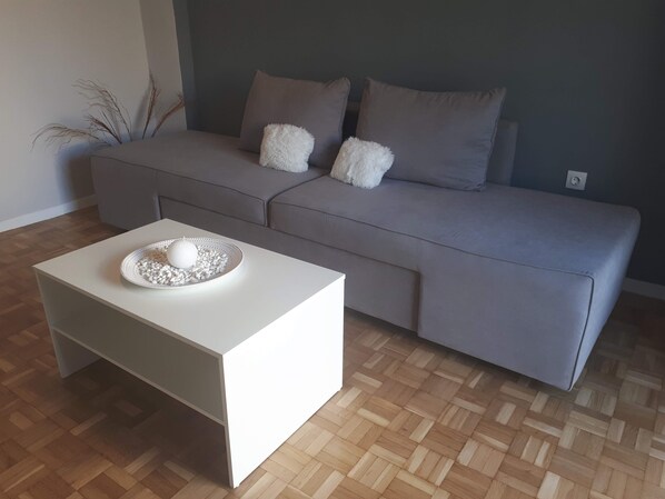 A modern living room with a grey sofa, a white coffee table, and a wooden parquet floor.