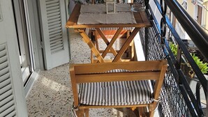 A balcony with a wooden table and chairs, a potted plant, and a black metal railing. - A nice apartment in corfu town (Corfu)