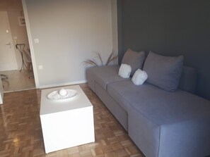 A modern living room with a grey sofa, two white fluffy cushions, and a white coffee table with a decorative item.
