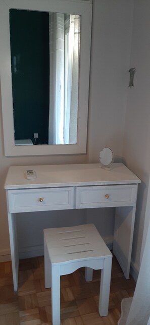 A white desk with two drawers and a small round mirror on top.