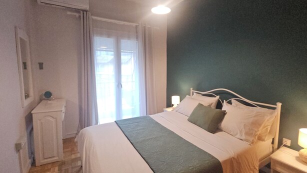 A bedroom with a bed, bedside tables, a nightstand, a window with curtains, and a door. - A nice apartment in corfu town (Corfu)