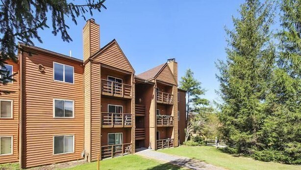 Un bâtiment en bois à deux étages, doté de balcons, d’une entrée centrale et d’une cour verdoyante.