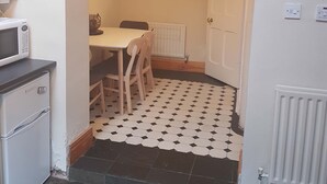A compact kitchen with a microwave, a small refrigerator, a dining table with chairs, and a patterned floor. - Delightful Victorian House (Belfast)