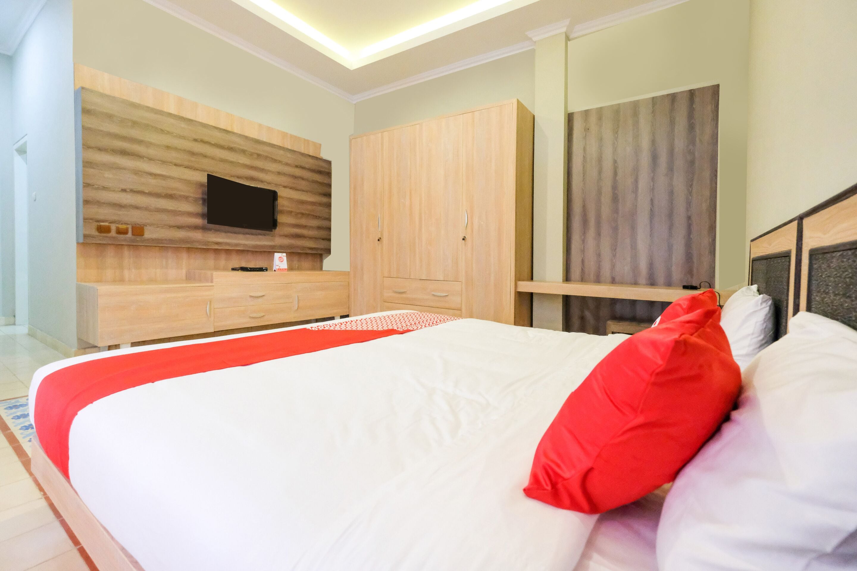 A bedroom with a bed, a TV mounted on the wall, wooden cabinets, and a mirror.