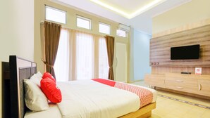 A hotel room with a bed, a TV mounted on the wall, a wooden dresser, and a window with curtains. - Super OYO Collection O 2383 Andongkoe 64 Salatiga (Salatiga)