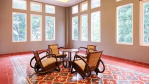 A room with a tiled floor, a round table with chairs, and large windows with a view of trees. - Super OYO Collection O 2383 Andongkoe 64 Salatiga (Salatiga)