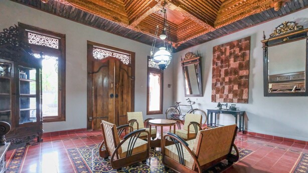 A traditional room with a wooden ceiling, a patterned floor, a round table with chairs, a bicycle, and a mirror. - Super OYO Collection O 2383 Andongkoe 64 Salatiga (Salatiga)