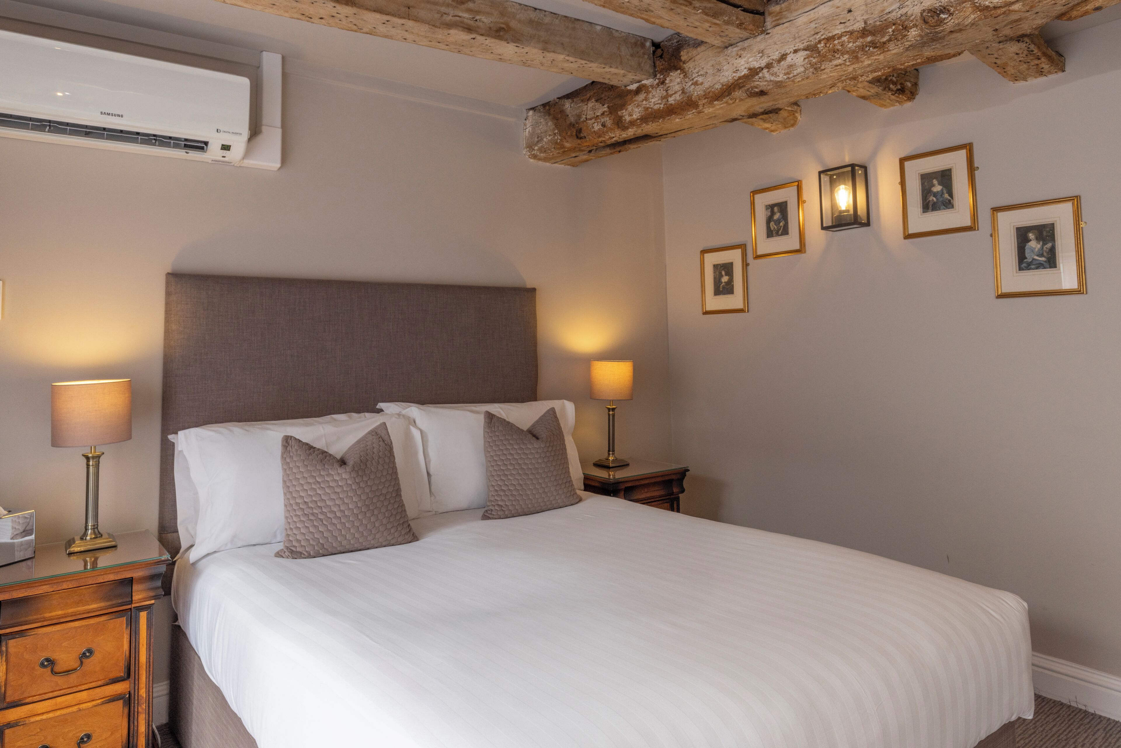Habitació d'hotel amb un llit gran, tauletes de nit, aire condicionat fixat a la paret i quadres emmarcades al mur.