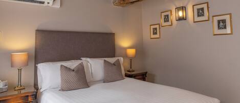 A hotel room with a large bed, bedside lamps, a wall-mounted air conditioner, and framed pictures on the wall.