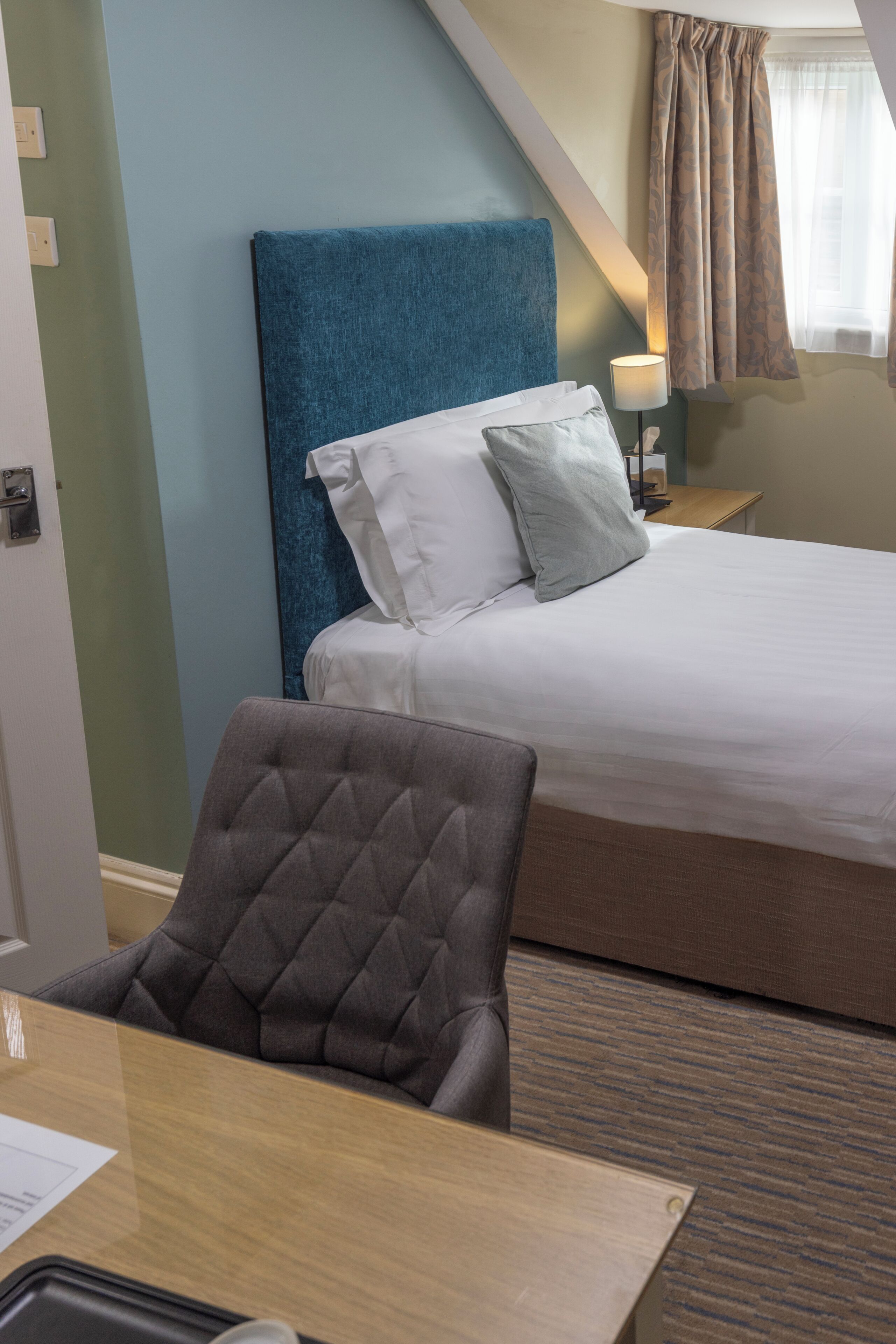 Una habitación de hotel con una cama, una silla, un escritorio y una lámpara.
