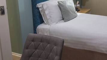 Una habitación de hotel con una cama, una silla, un escritorio y una lámpara.