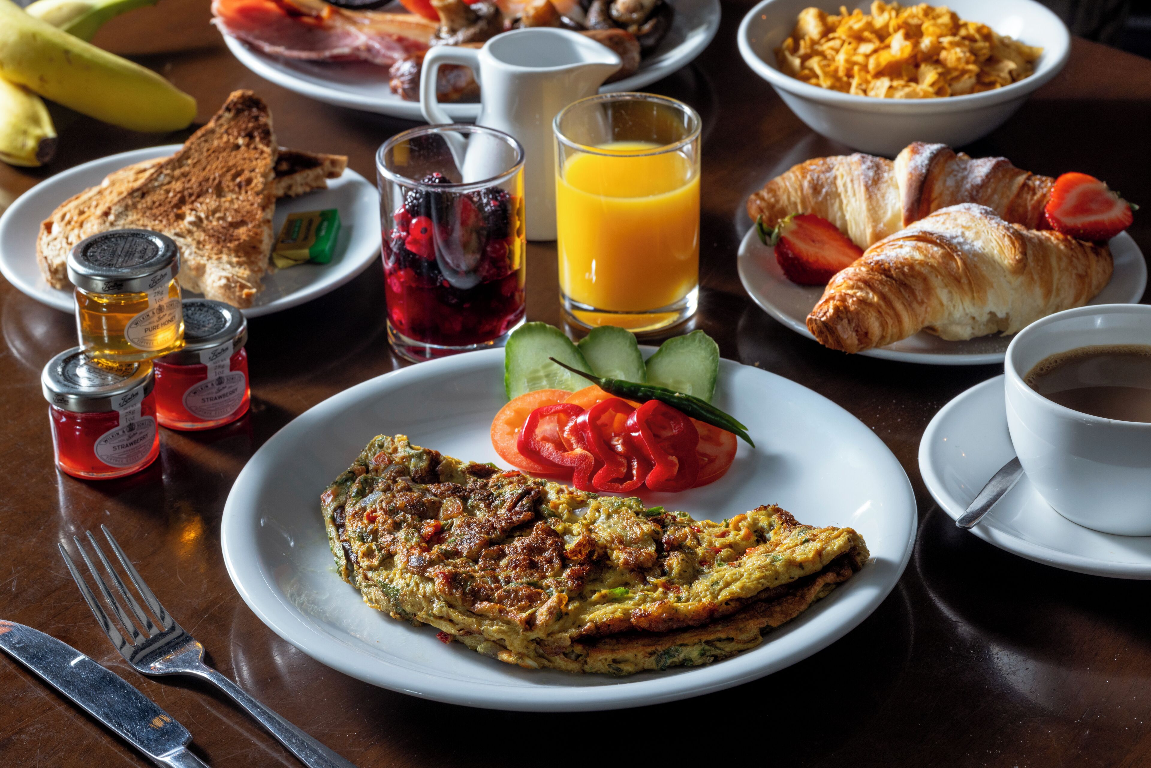 A breakfast setting with toast, a plate of vegetables, a croissant, a glass of orange juice, and a cup of coffee.