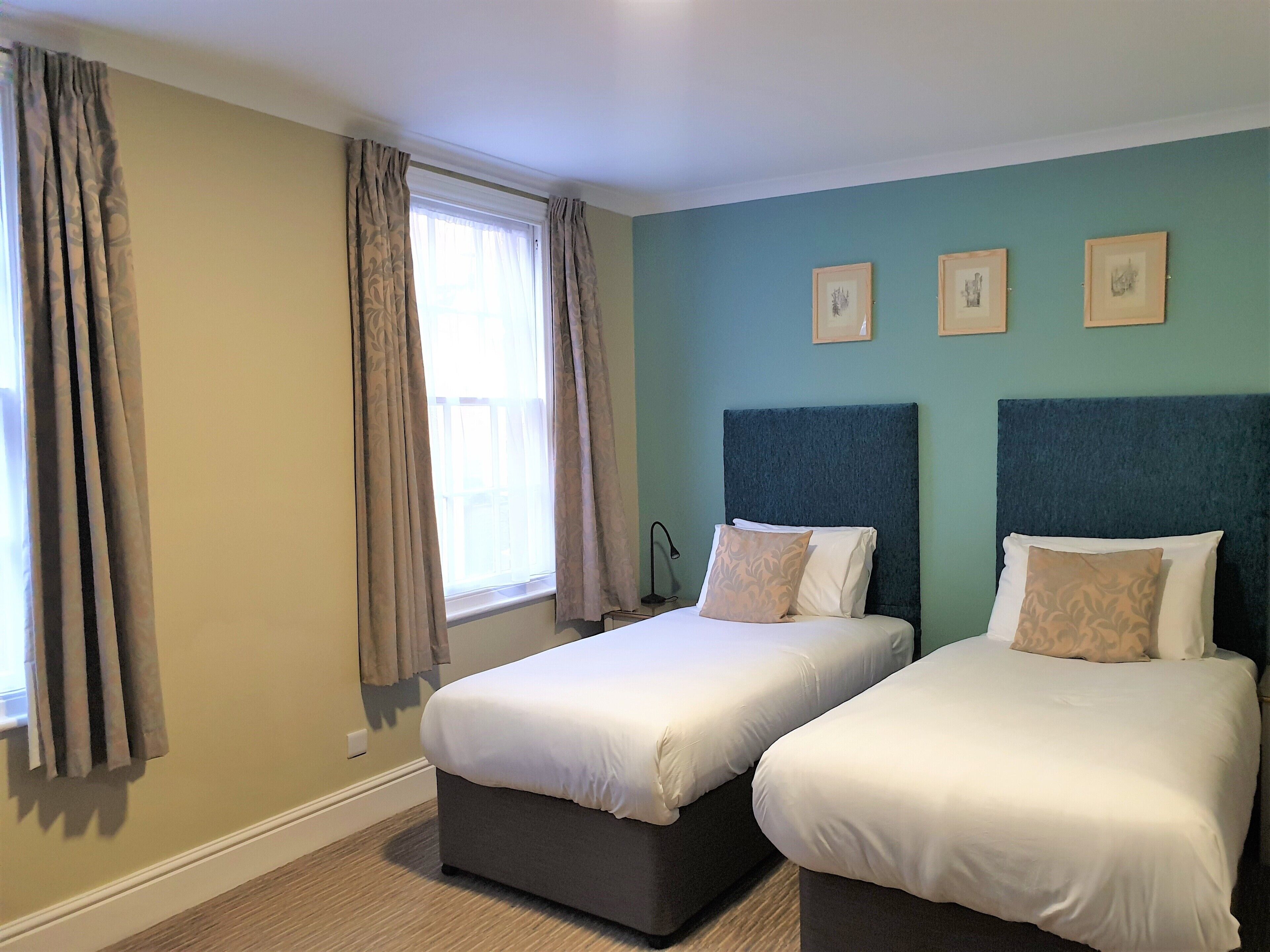 A hotel room with two beds, a window with curtains, and three framed pictures on the wall.