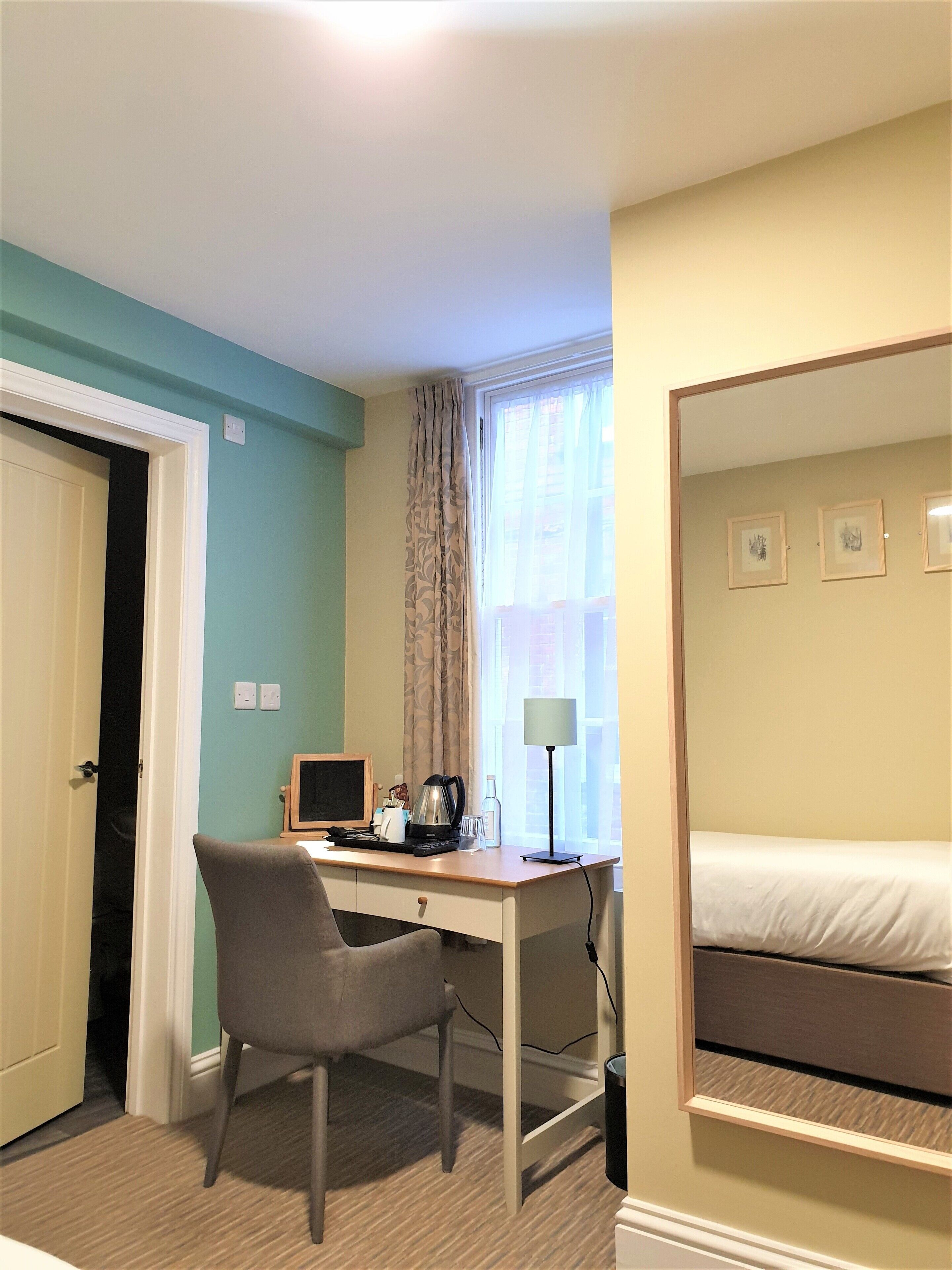 A hotel room with a desk, chair, computer, lamp, and a bed.