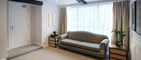 A cozy living room with a plaid sofa, a small side table, a potted plant, and a door leading to another room.