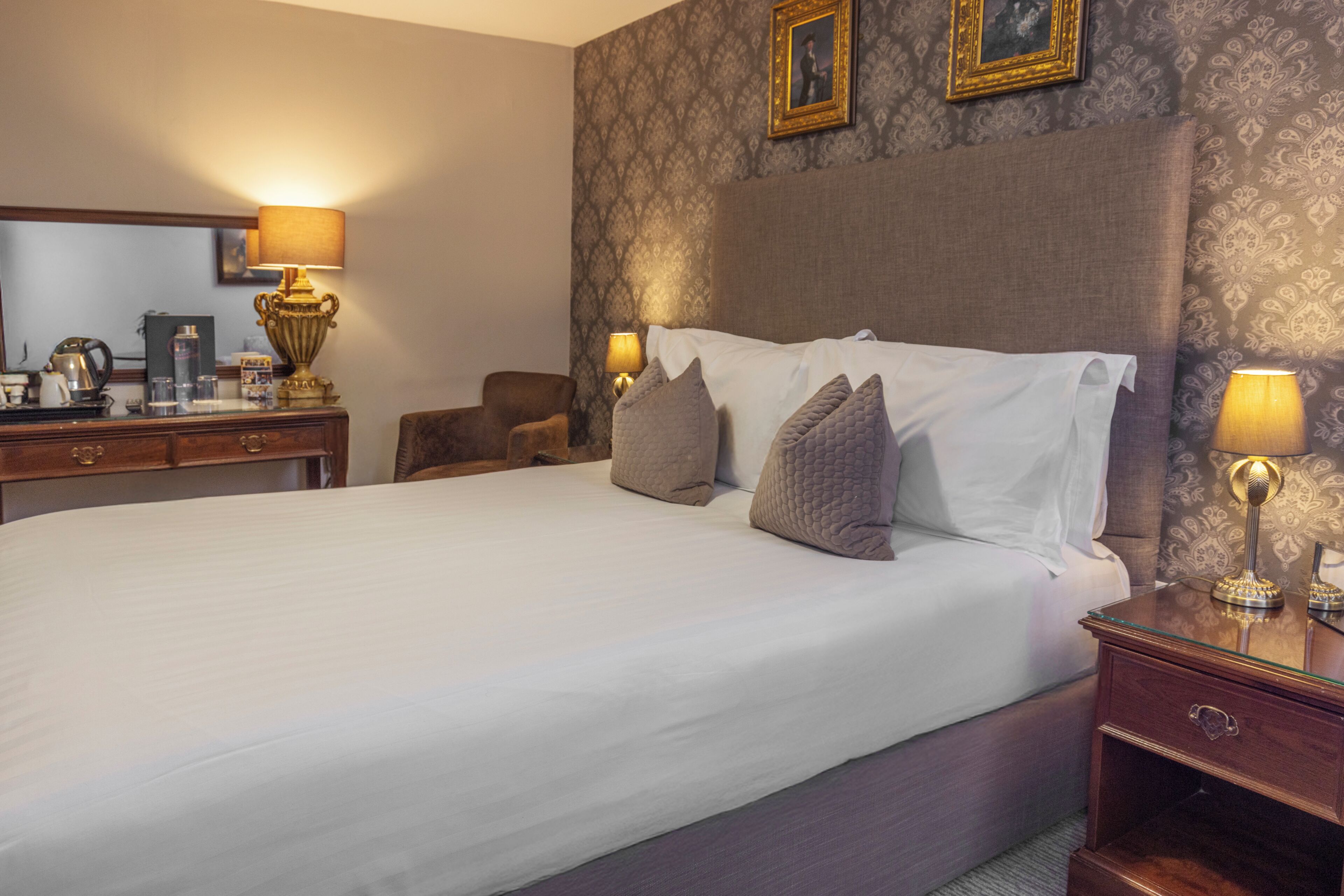 Una habitación de hotel con una cama grande, un aparador de madera, una silla y dos lámparas de noche.