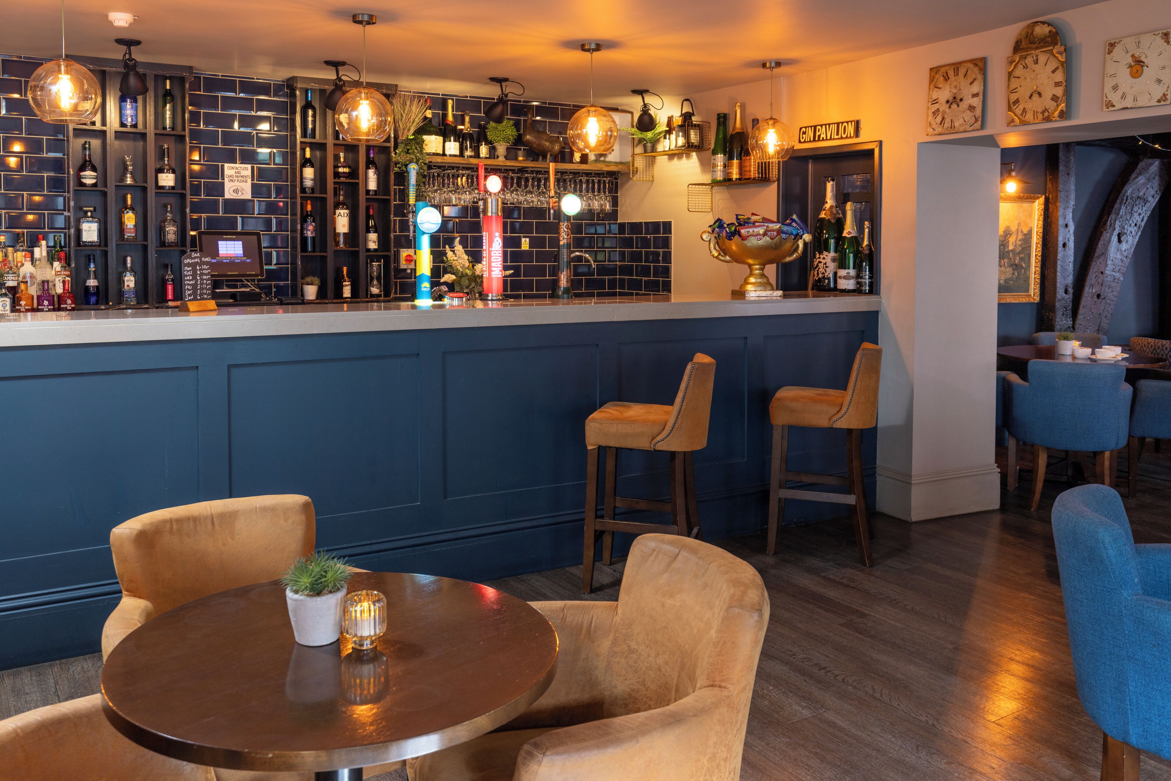 Un espace bar comprenant un comptoir, des tabourets de bar et un coin salon avec une table ronde et des chaises.