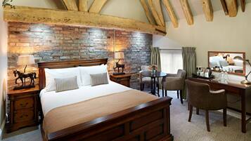 Une chambre avec un mur en briques, des poutres en bois au plafond, un grand lit, un bureau et une chaise.