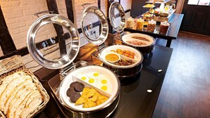 Tarjolla on monipuolinen buffet, jossa on erilaisia ruokia ja niitä varten tarkoitettuja astioita.
