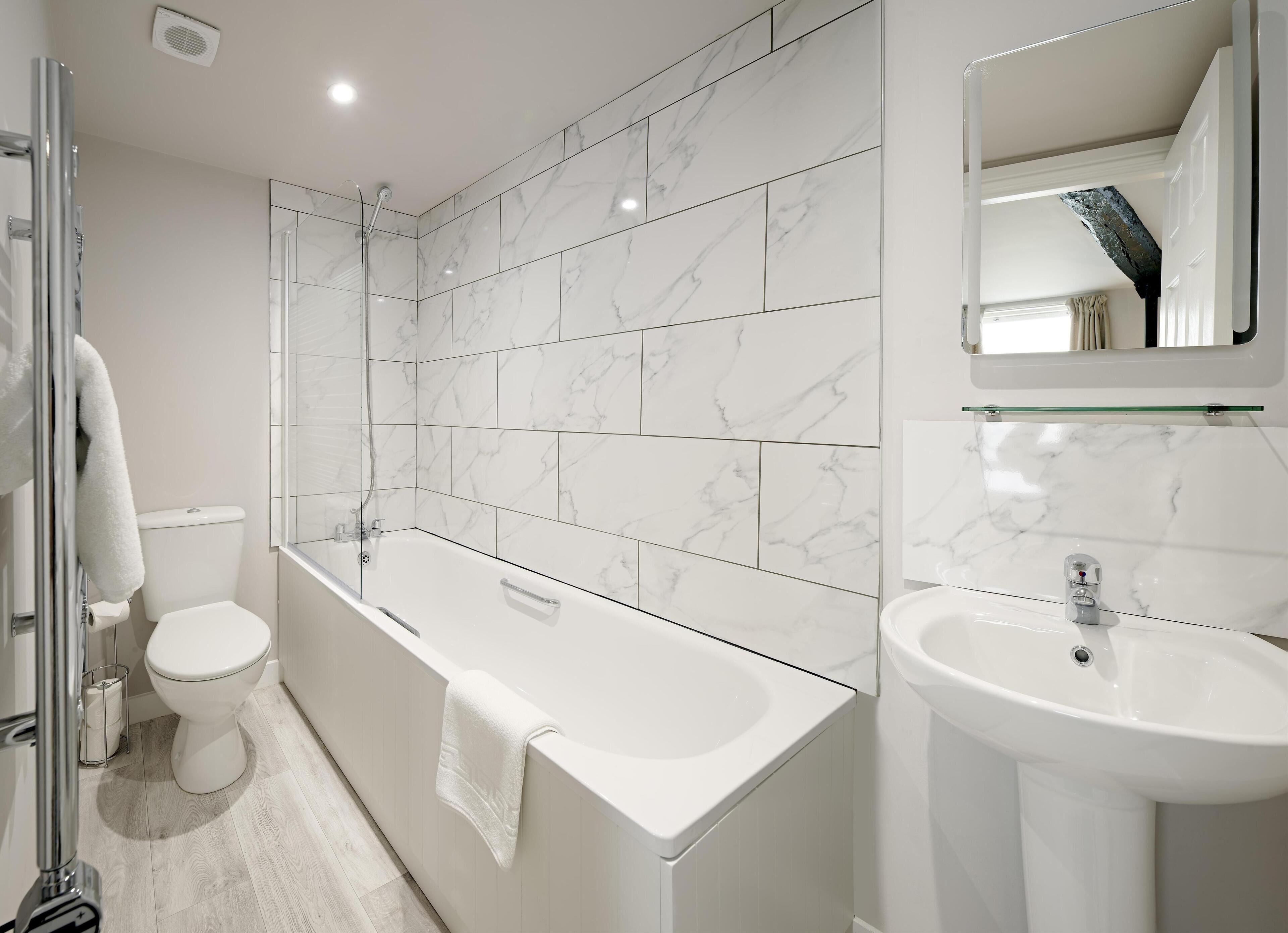 A modern bathroom with a glass shower enclosure, a freestanding bathtub, a toilet, and a pedestal sink.