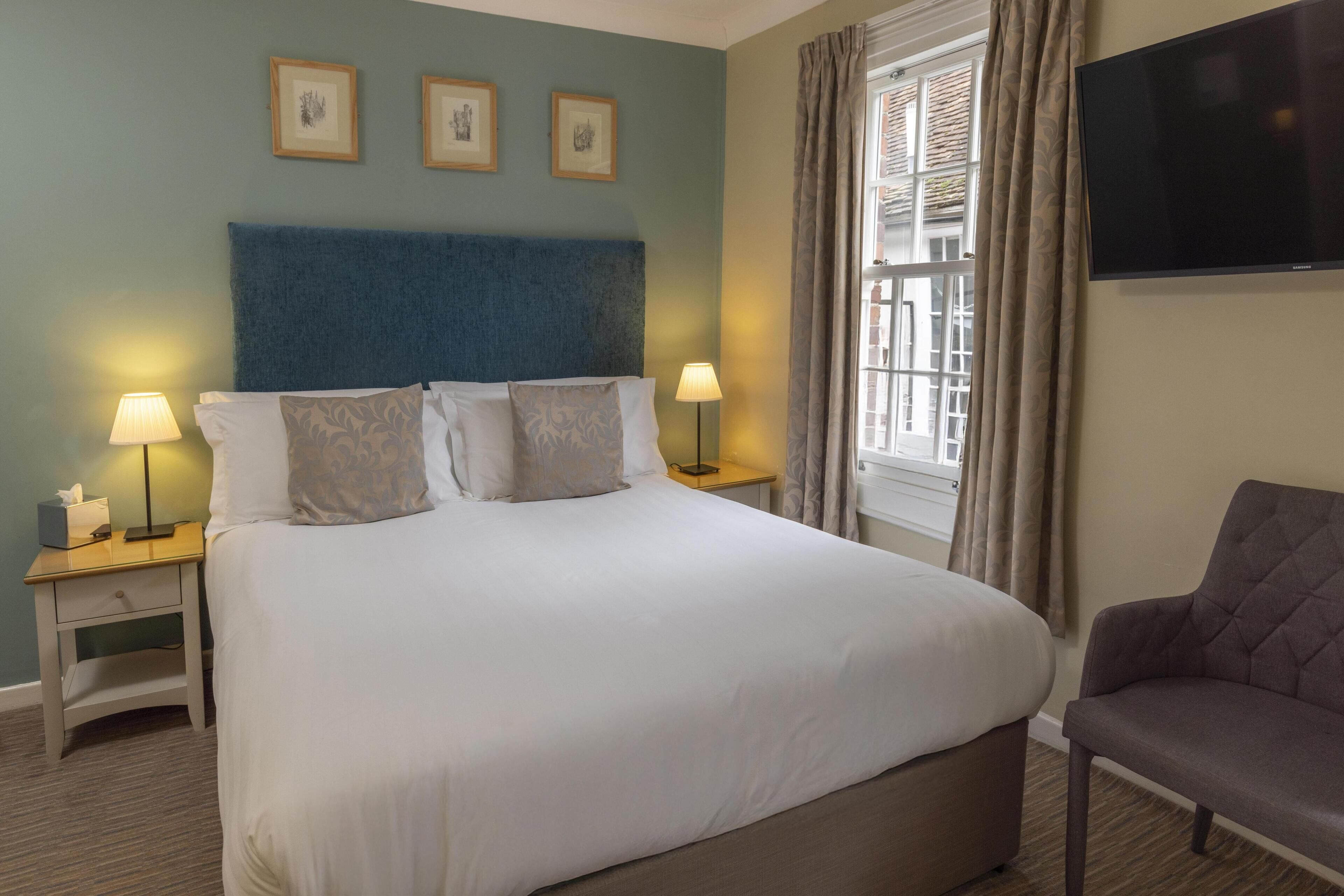 Habitación de hotel con una cama grande, dos mesitas de noche con lámparas, un televisor de pantalla plana y una ventana con cortinas.