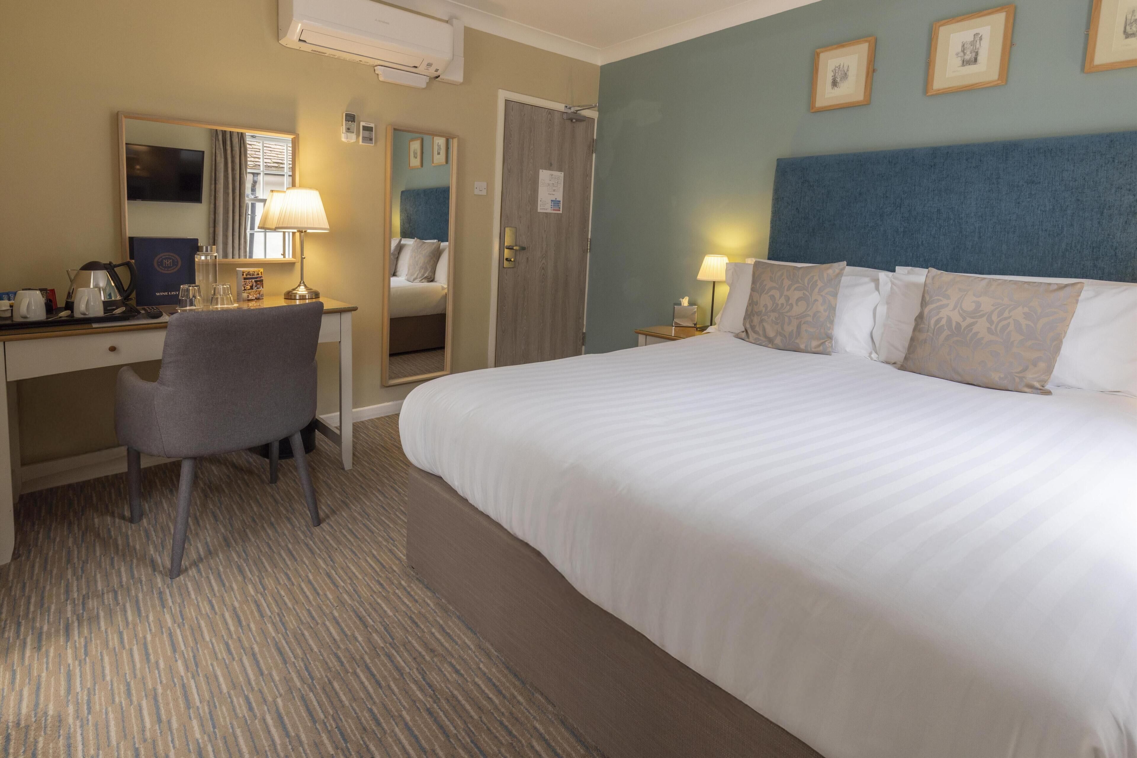 A hotel room with a bed, desk, chair, and a mirror.