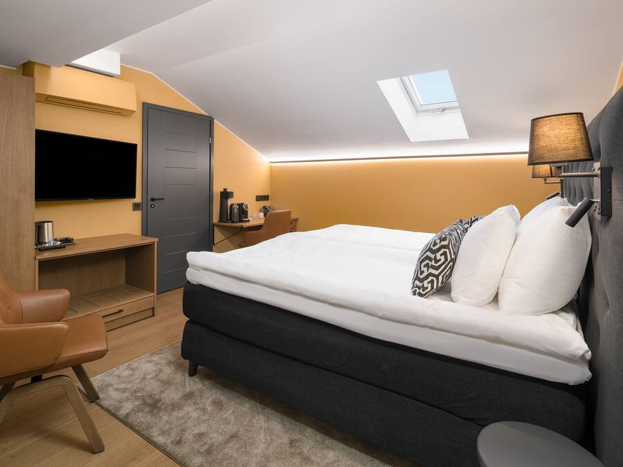 A modern bedroom with a bed, desk, chair, and a TV.