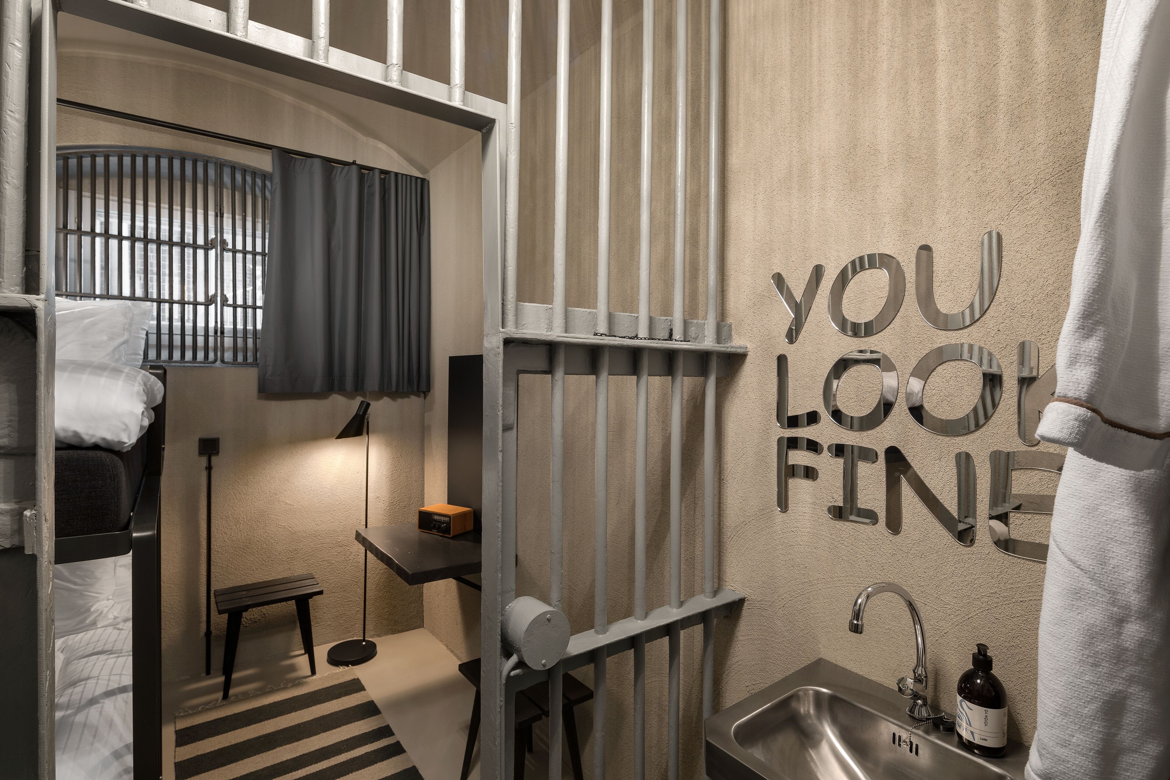Habitación de hotel compacta con literas, un escritorio pequeño, un lavabo y un espejo.