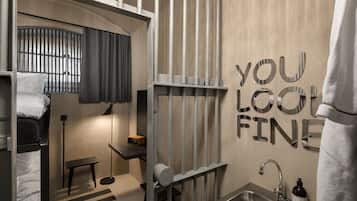 A compact hotel room with a bunk bed, a small desk, a sink, and a mirror.